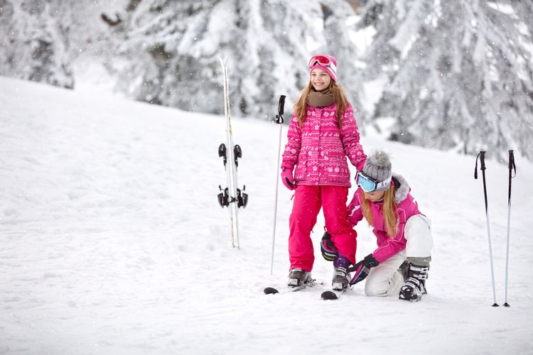 Matka pomáhá dceři připevnit lyžařku o lyže