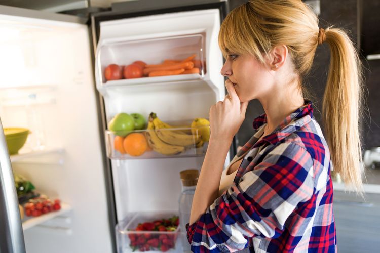 Mladá žena přemýšlí nad jídlem v chladničce